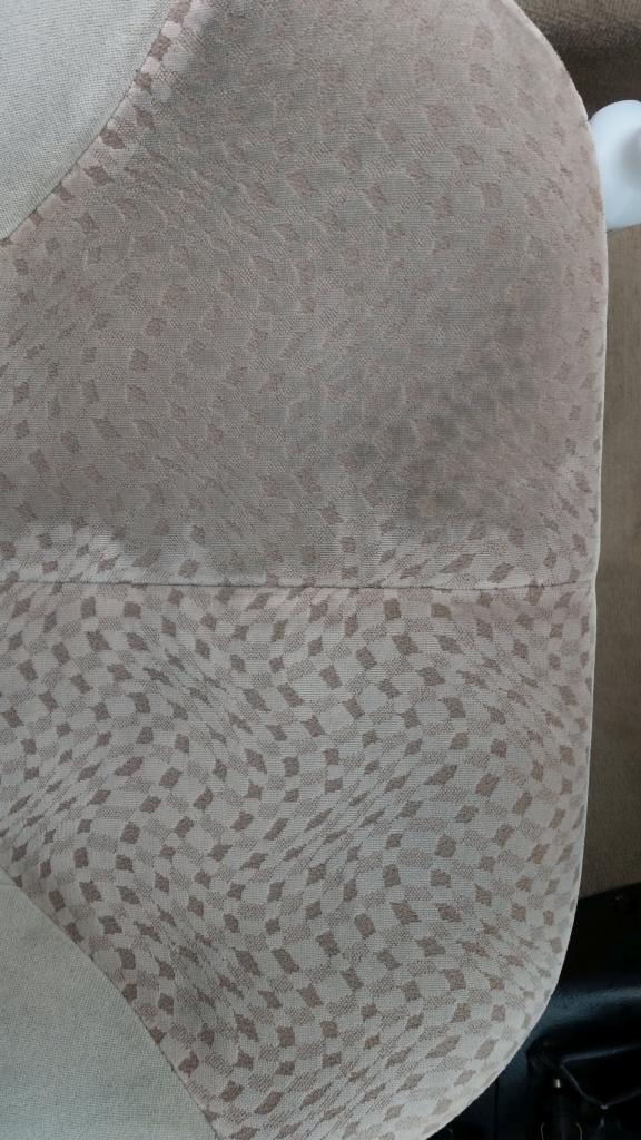 Fragment tapicerki krzesła lub kanapy w odcieniach beżu z geometrycznym wzorem, widoczny szew łączący dwie części materiału.