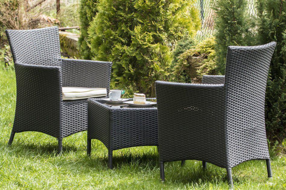 Zestaw mebli ogrodowych z plecionki technorattanowej: dwa fotele z poduszkami i stolik kawowy z filiżanką i ciastkiem, na trawniku w ogrodzie.