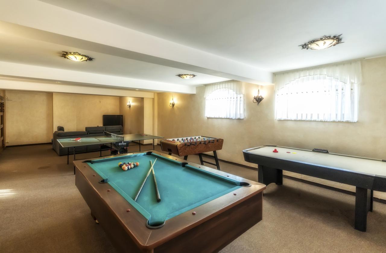 Pokój rekreacyjny z bilardem, stołem do ping-ponga, piłkarzykami i cymbergajem, oświetlony ozdobnymi lampami, z sofą w tle.
