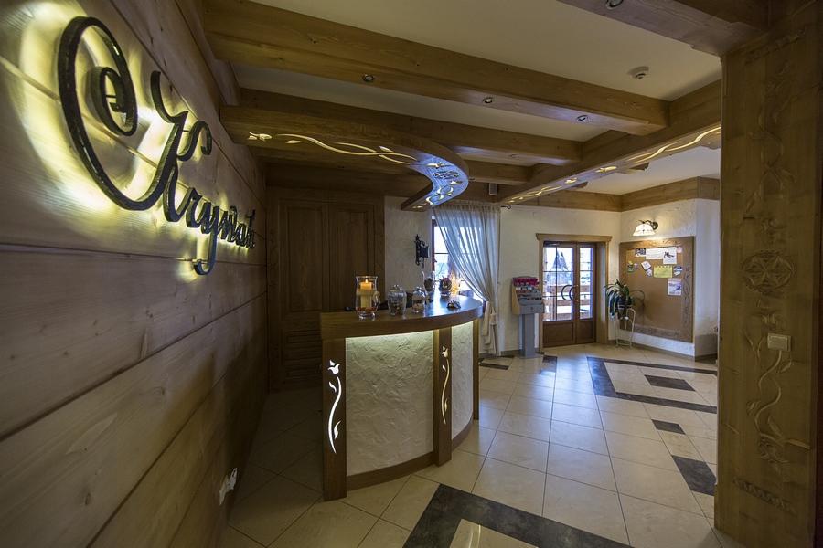 Recepcja hotelowa z drewnianymi elementami dekoracyjnymi, podświetlanym napisem 'Kryształ' i widokiem na wejście.