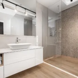 Nowoczesna łazienka z kabiną prysznicową typu walk-in, umywalką nablatową na białej szafce, drewnopodobną podłogą z oświetleniem LED i ścianą z mozaiki 3D.