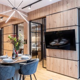 BB Fabrik - Nowoczesne wnętrze z drewnianą okładziną ścian, czarnymi ramami szklanych drzwi i okien, okrągłym stołem z szarymi krzesłami i designerską lampą sufitową.