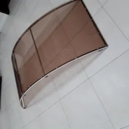 Brązowy, łukowaty daszek z metalową ramą, leżący na jasnych płytkach podłogowych.