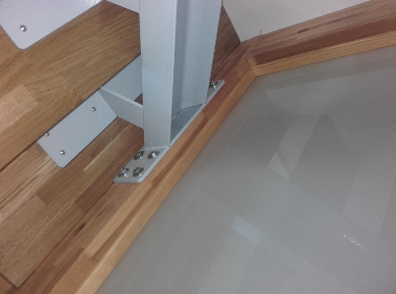 Stalowa konstrukcja schodów przymocowana do drewnianych stopni i podłogi za pomocą śrub, widok z dołu.