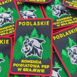 Naszywki z haftowanym logo Komendy Powiatowej PSP w Grajewie na tle zielonych drzew, wykonane w Grajewie.