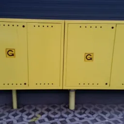 Żółta, podwójna szafka gazowa z logo firmy na elewacji budynku z szarą podmurówką i betonową kostką brukową.