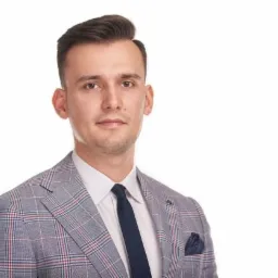 Portret młodego mężczyzny w garniturze w kratę i granatowym krawacie na białym tle, reprezentującego doradcę finansowego z Opola.