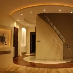 Wykończone wnętrze z podświetlanym sufitem, drewnianą podłogą z okrągłym wzorem i zamontowanym uchwytem na telewizor, widoczna drabina oparta o ścianę.