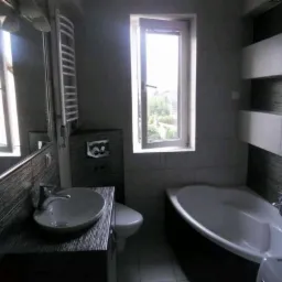 Nowoczesna łazienka z ciemnymi płytkami imitującymi drewno na ścianach, białą armaturą i oknem z widokiem na zieleń, prezentująca minimalistyczny styl.