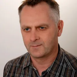 Portret mężczyzny w koszuli w kratę, z krótkimi, lekko postawionymi włosami i niebieskimi oczami, spoglądającego w lewo.