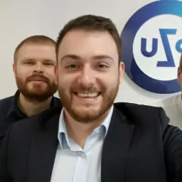 Trzech uśmiechniętych mężczyzn w biurze, z logo firmy w tle, zdjęcie typu selfie.