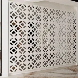 Biała szafa wnękowa z ażurowymi drzwiami o geometrycznym wzorze, widoczna na tle jasnego wnętrza z marmurową podłogą i czarnymi ramami drzwi.