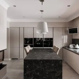 Elegancka kuchnia w odcieniach beżu z wyspą z czarnego marmuru, zabudowane sprzęty AGD, nowoczesny kominek i roleta rzymska w oknie.