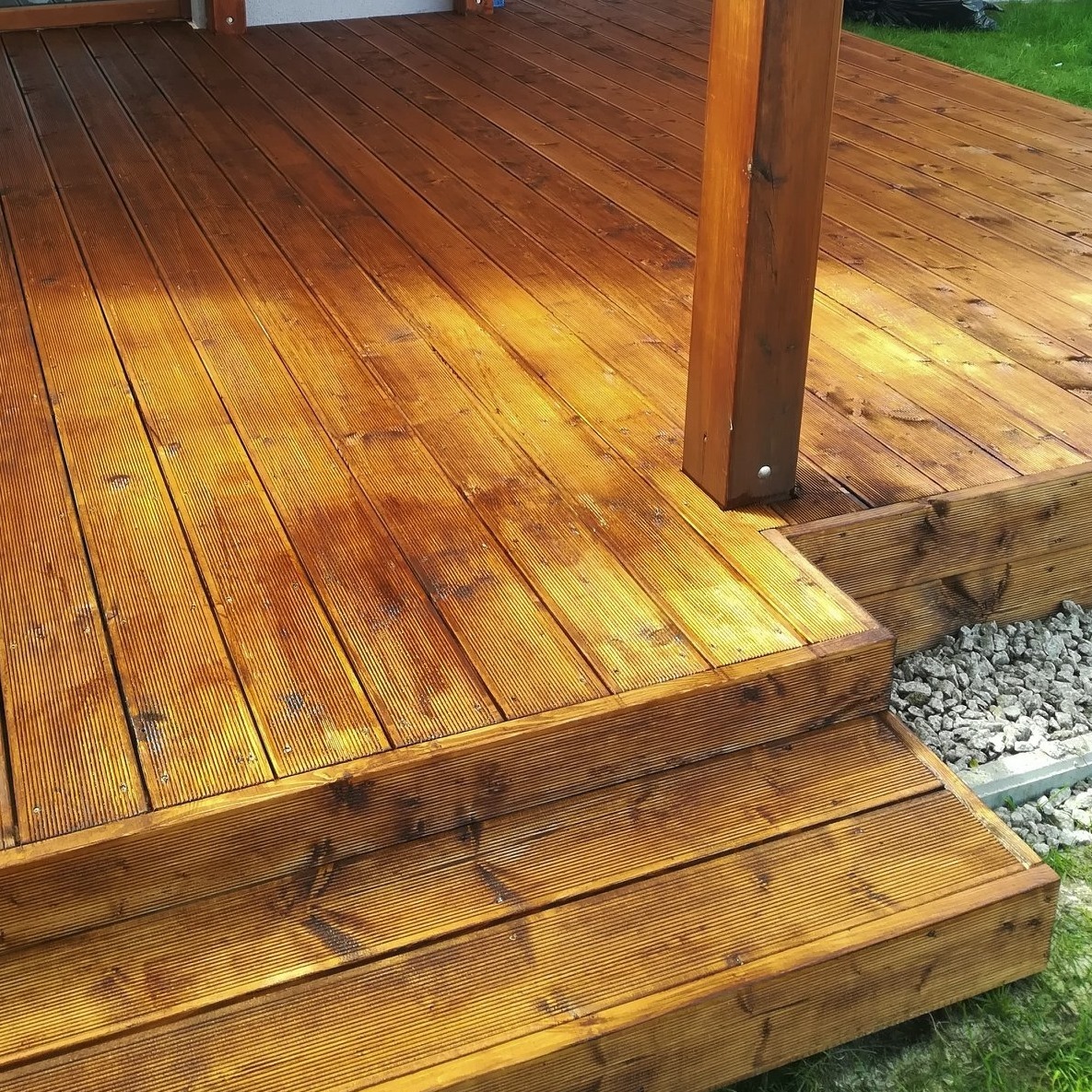 Nowo zaimpregnowany taras z drewna egzotycznego ze schodami, widoczny fragment filaru i otoczenie z kamieni ozdobnych.