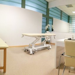 Centrum medyczne Olimedica - Jasne wnętrze gabinetu z dwoma leżankami, biurkiem z laptopem HP i kwiatami, widoczne elementy wyposażenia medycznego.