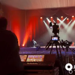 Kamera filmowa na statywie i konsoleta oświetleniowa z monitorem w Płońsku, podczas przygotowań do wydarzenia na scenie z czerwonym oświetleniem.