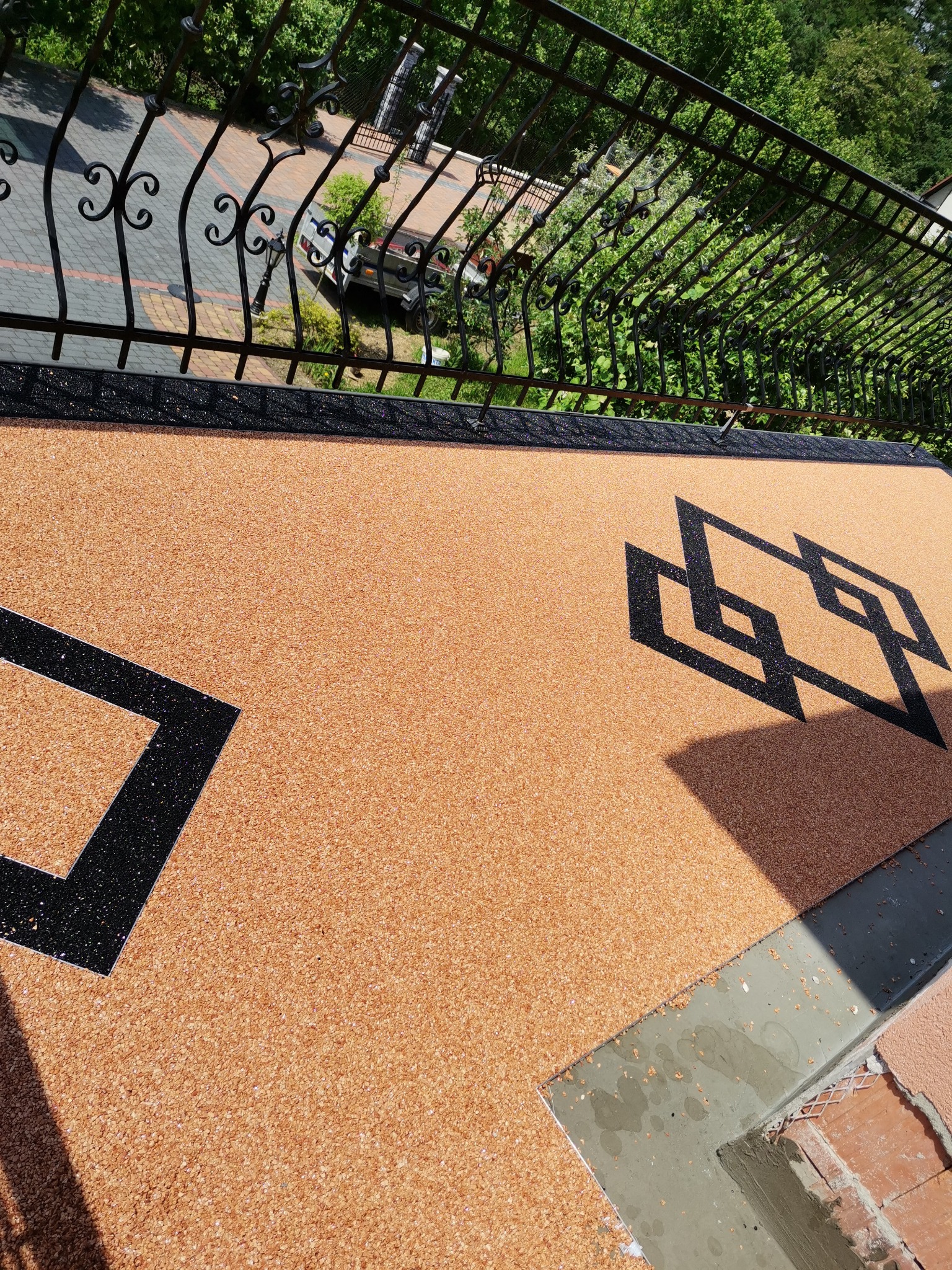 Wykończona powierzchnia balkonu z żywicy epoksydowej w kolorze piaskowym z czarnym geometrycznym wzorem, widok z góry na balustradę i otoczenie