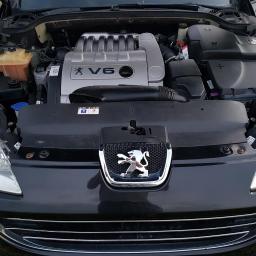 DC Auto - Otwarta maska czarnego samochodu Peugeot z widocznym silnikiem V6, potencjalnie przygotowywanym do montażu instalacji autogaz.