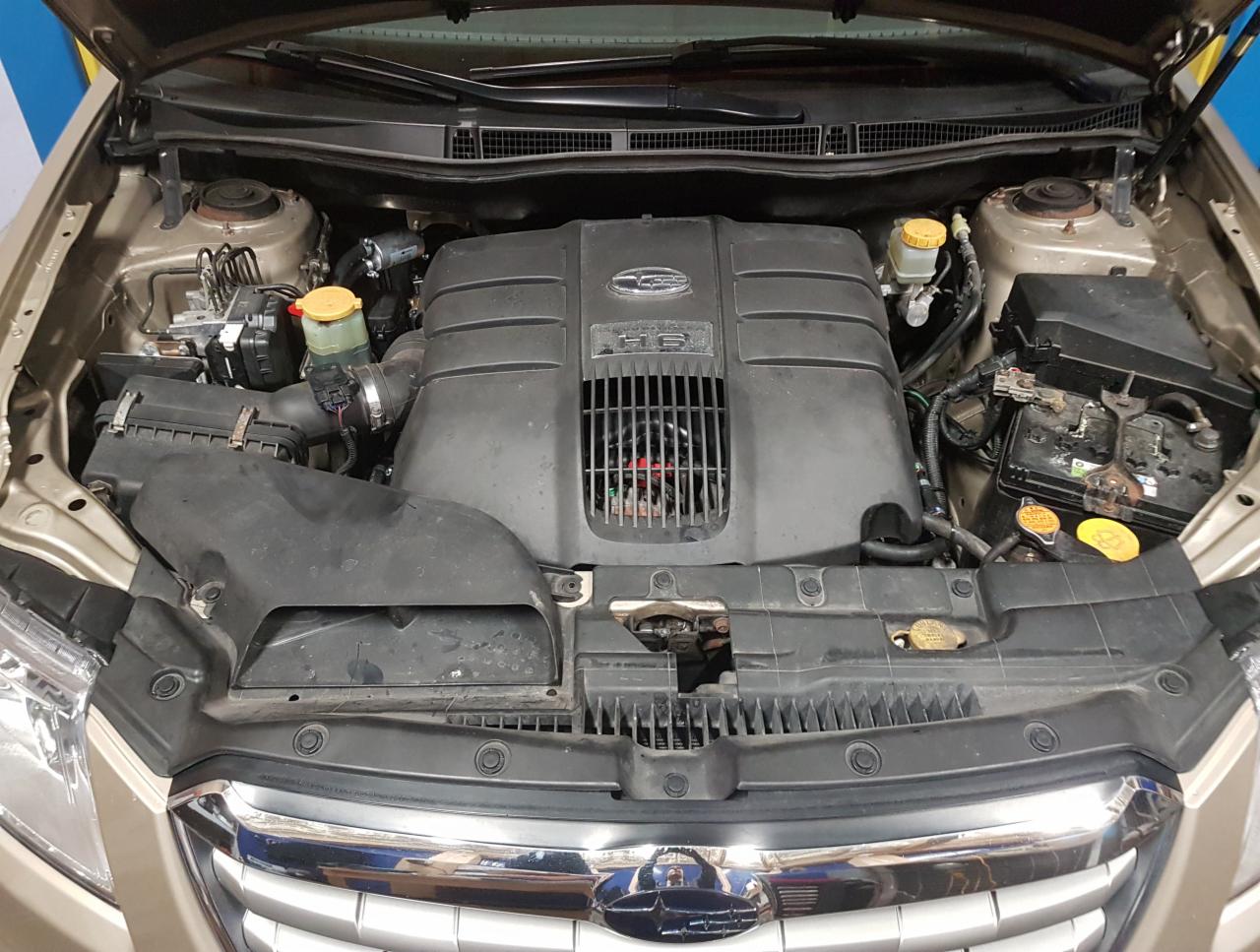 Otwarta maska samochodu, widoczny silnik Subaru H6 z elementami instalacji zasilania alternatywnego, widoczne przewody i zbiorniczki płynów.