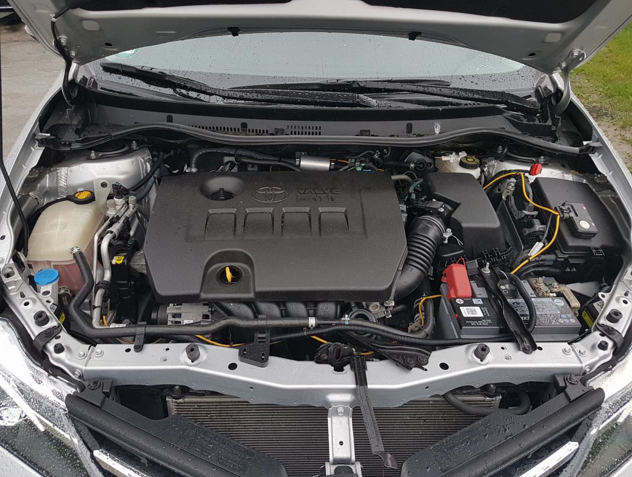 Silnik samochodu marki Toyota z otwartą maską, widoczny akumulator, zbiornik płynu chłodniczego i inne elementy układu napędowego.