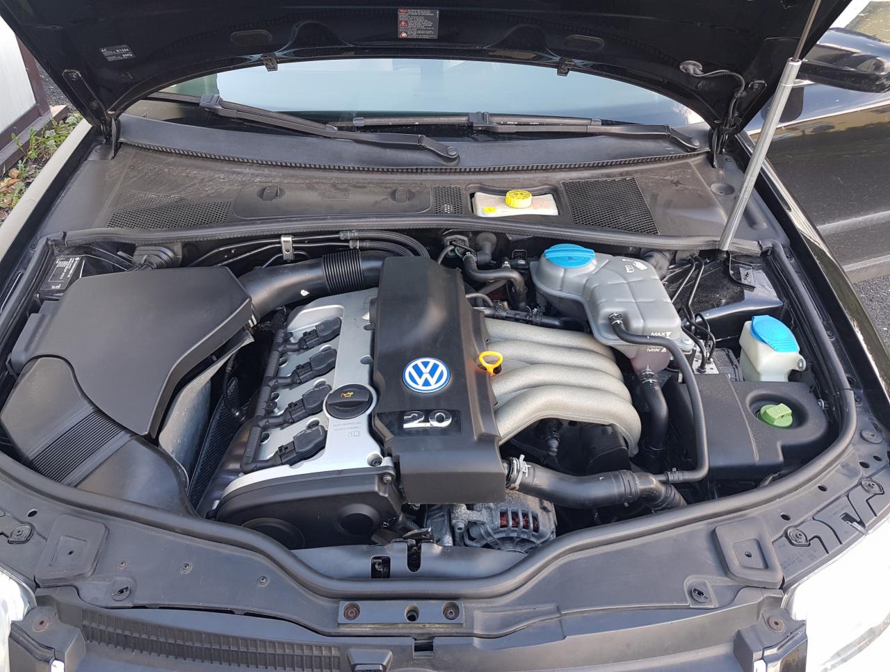 Otwarta maska czarnego samochodu marki Volkswagen, widoczny silnik benzynowy 2.0 z instalacją gazową, zbiorniki płynów chłodniczych z niebieskimi nakrętkami.