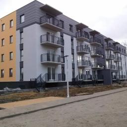 Usługi Ogólnobudowlane Dawid Plesner - Nowoczesny budynek wielorodzinny z balkonami, wykończony w odcieniach szarości i żółci, widoczny fragment terenu przed budynkiem w trakcie prac wykończeniowych.