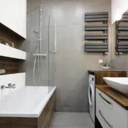Nowoczesna łazienka z wanną obudowaną drewnem, szklanym parawanem nawannowym, szarymi płytkami, grzejnikiem drabinkowym, białą umywalką nablatową i pralką ukrytą w zabudowie.