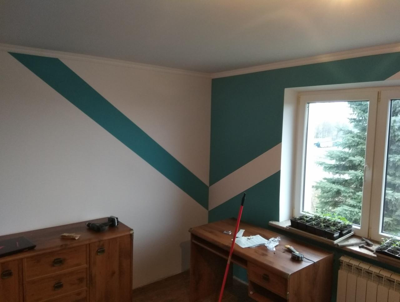 Pomieszczenie po malowaniu ścian z geometrycznym wzorem w kolorze morskim, widoczne meble i narzędzia malarskie oraz sadzonki roślin na parapecie okna.