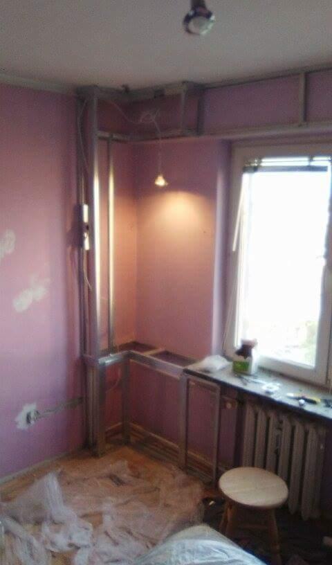 Łazienka w Grzęsce w trakcie prac remontowych: widoczne metalowe profile konstrukcyjne, częściowo zabudowana wanna, osłonięta podłoga, okno z grzejnikiem i narzędziami na parapecie.