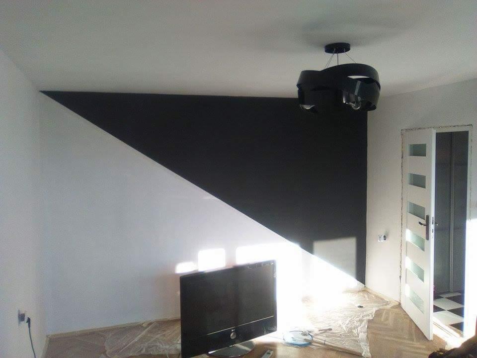 Pokój po malowaniu z geometrycznym podziałem ściany na białą i czarną, nowoczesna lampa sufitowa i białe drzwi z przeszkleniami, widoczne zabezpieczenia podłogi folią malarską.