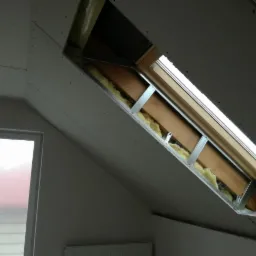 Montaż okna dachowego w skośnym poddaszu z widoczną izolacją wełną mineralną i płytami gipsowo-kartonowymi przed szpachlowaniem.