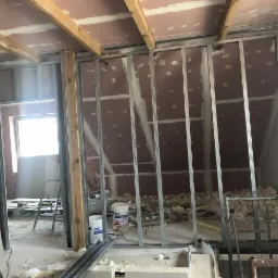 Konstrukcja metalowa pod zabudowę poddasza z widocznymi płytami gipsowo-kartonowymi na skośnej ścianie, częściowo ocieplona, z widocznymi fragmentami wełny mineralnej i wiadrami z masą szpachlową...