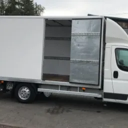 Biały samochód dostawczy z otwartymi przesuwnymi drzwiami bocznymi, zaparkowany we Wrocławiu, widoczne zabezpieczenia ładunku wewnątrz, rampa załadunkowa opuszczona.