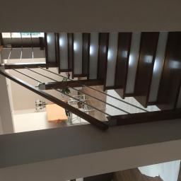 HAŁYS-Meble - Wnętrze domu z widokiem na schody z drewnianymi stopniami i metalowymi poręczami, oświetlone światłem wpadającym przez okno na górze.