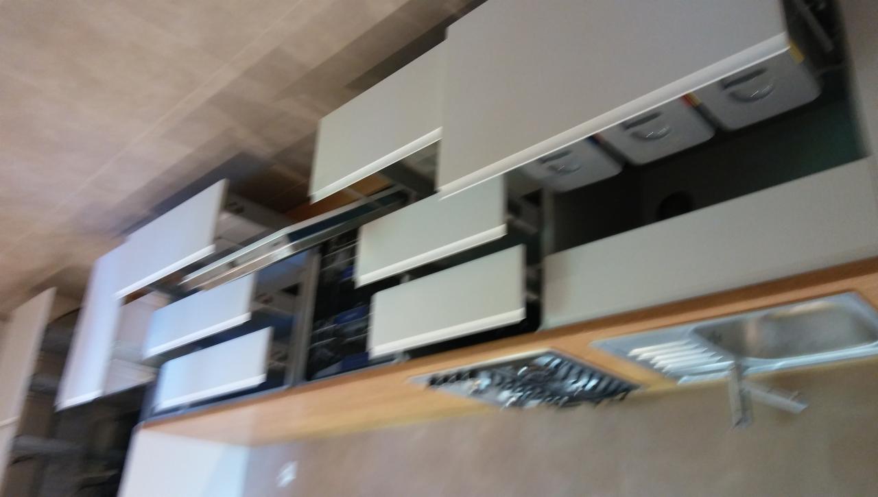 Nowoczesna kuchnia na wymiar z białymi frontami szafek, drewnianym blatem, zlewem i płytą gazową, widok z dołu, niedoskonałe oświetlenie.