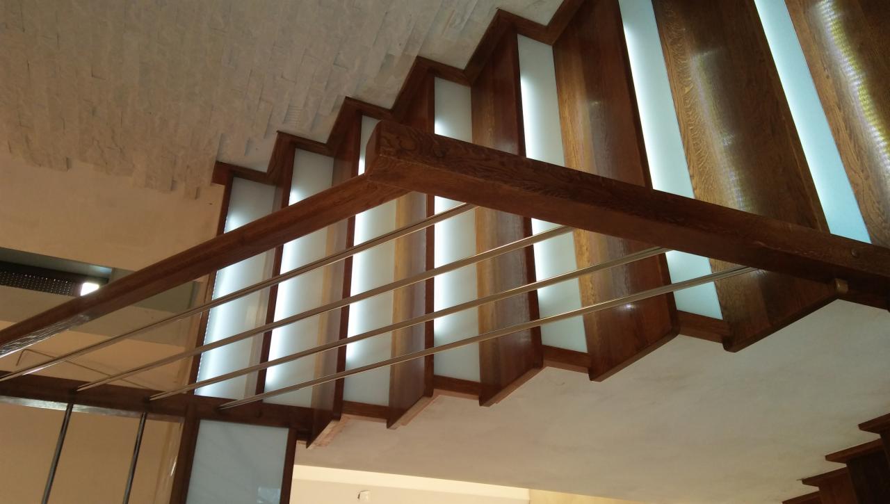 Nowoczesne schody drewniane z podświetlanymi stopniami i metalową balustradą, widok od dołu.