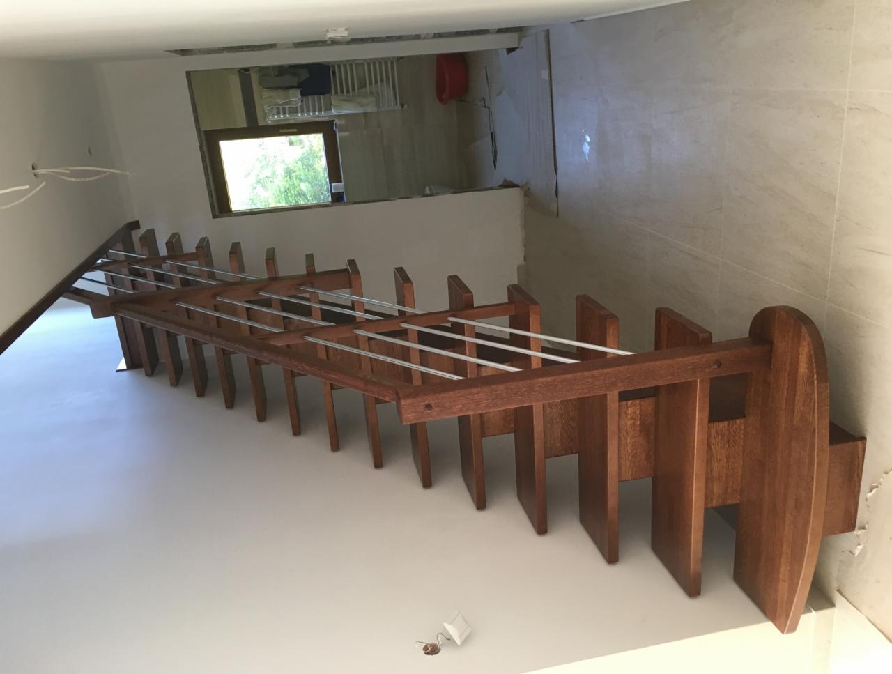 Surowe drewniane schody z metalowymi prętami, widok z dołu na tle białej ściany i okna w oddali.