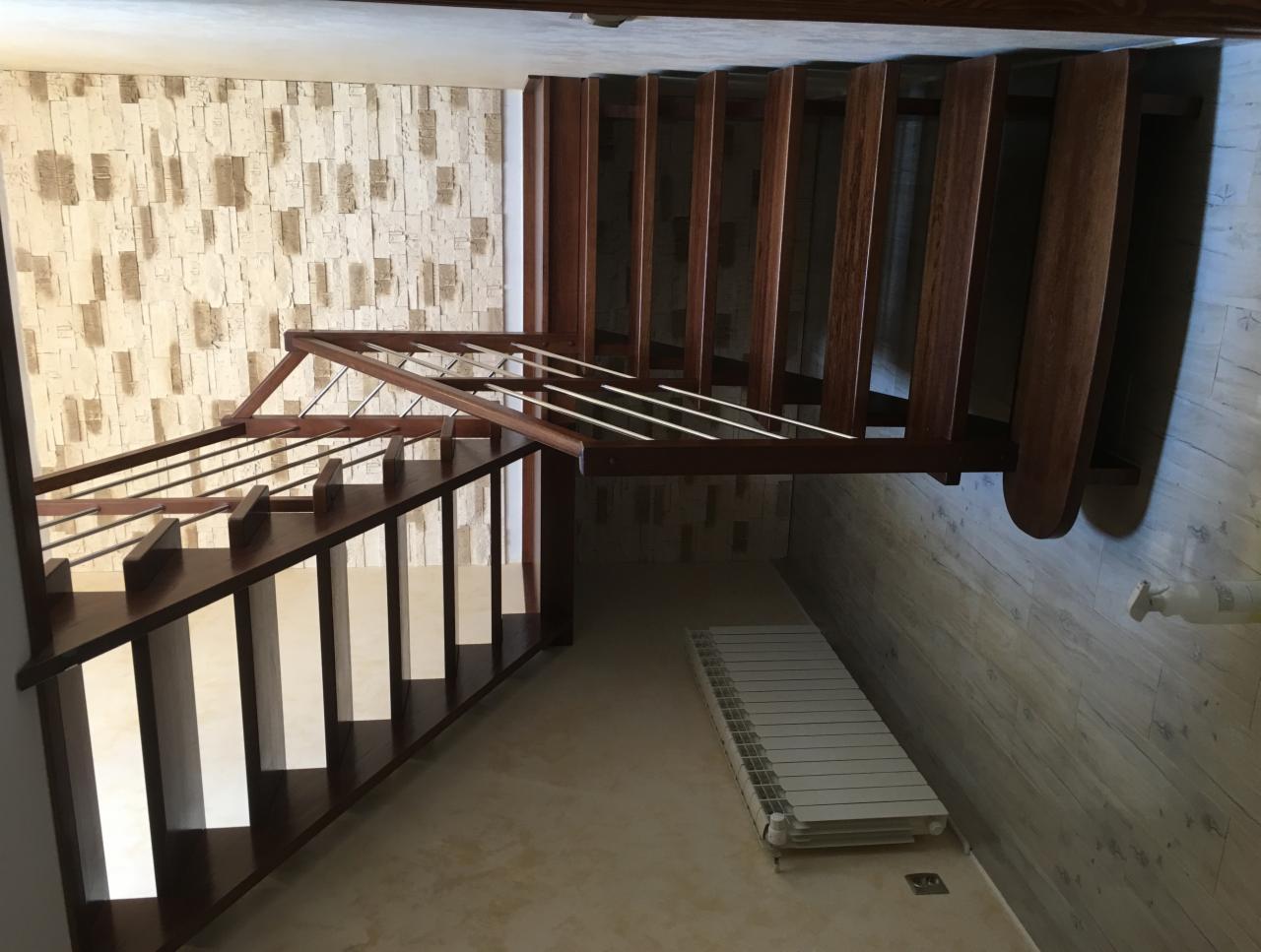Ciemnobrązowe schody z drewnianymi stopniami i metalowymi barierkami, widok z dołu, ściana z dekoracyjną tapetą w tle.