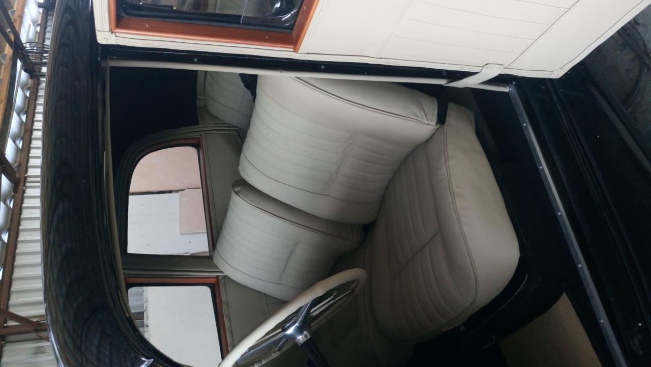 Wnętrze odrestaurowanego samochodu z jasną, skórzaną tapicerką siedzeń z przeszyciami, widoczna kierownica i fragment okna, czarna karoseria.