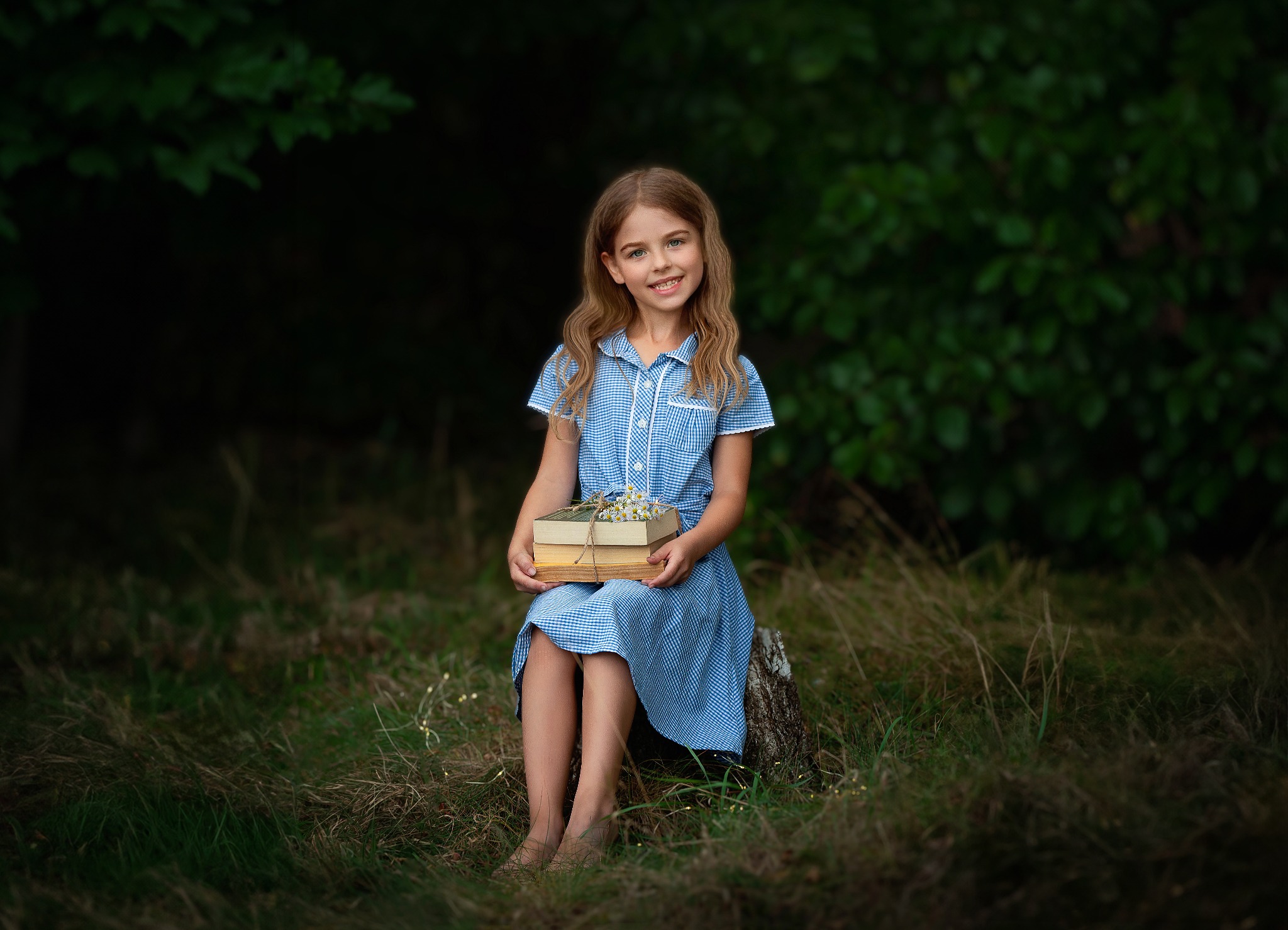 Dziewczynka w niebieskiej sukience siedzi na pniu drzewa, trzymając w rękach książki przewiązane sznurkiem i bukietem polnych kwiatów, na tle ciemnego lasu.