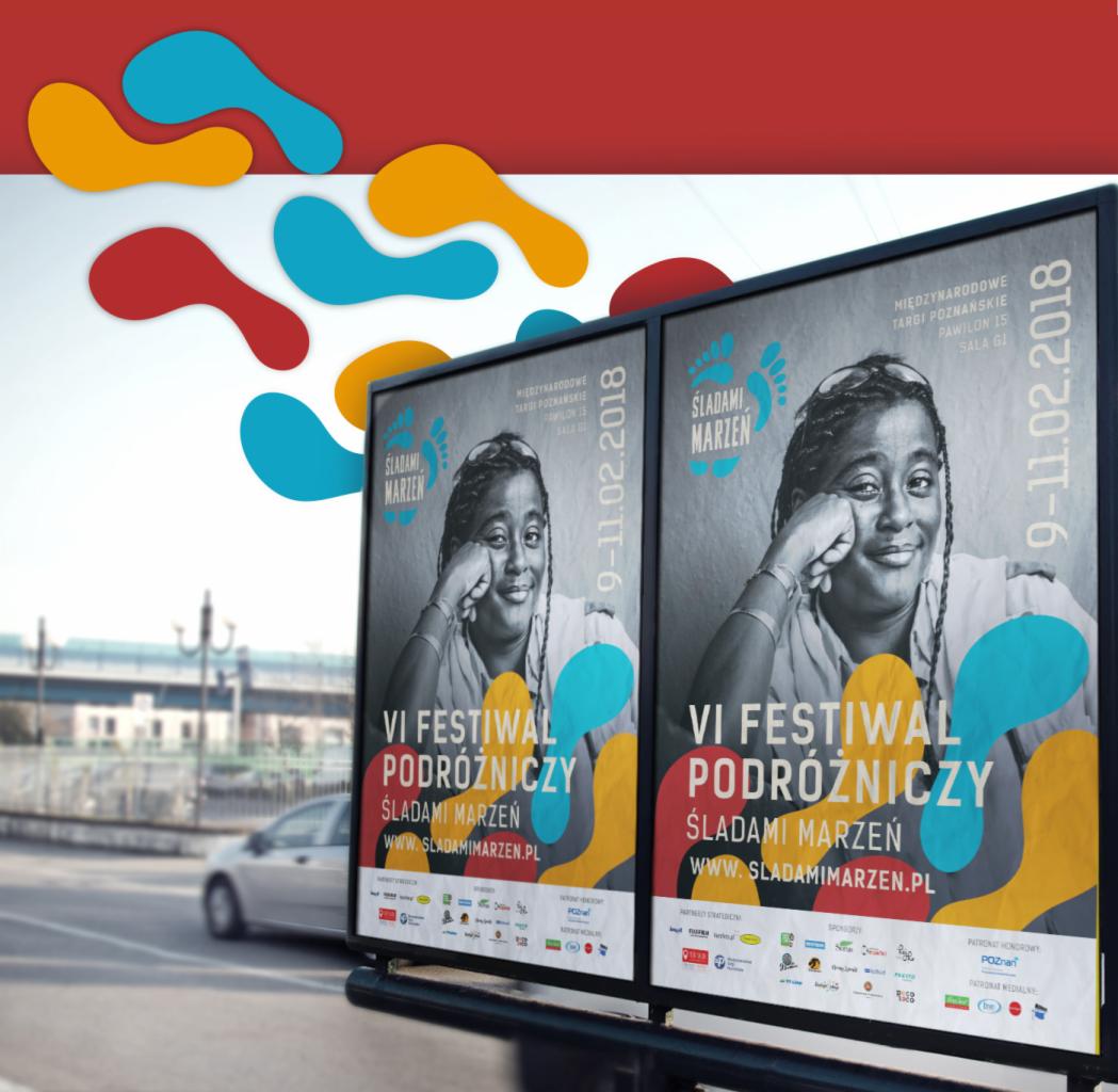 Billboard z plakatem VI Festiwalu Podróżniczego Śladami Marzeń, z portretem uśmiechniętej kobiety, ustawiony przy ulicy z widocznym samochodem w tle.