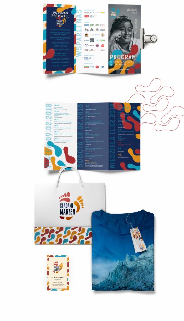 Zestaw materiałów promocyjnych festiwalu podróżniczego Śladami Marzeń, zawierający ulotkę, torbę z logo, wizytówkę i koszulkę z motywem górskim oraz metką festiwalową.