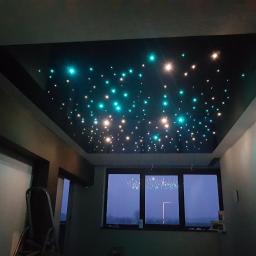 Maksimus - Czarny sufit podwieszany z oświetleniem LED imitującym gwiazdy, widok z dołu, drabina oparta o ścianę po lewej stronie, okno w tle.