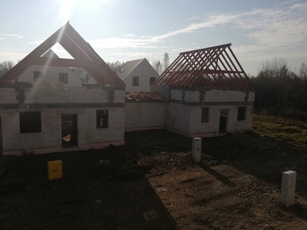 Budowa zespołu budynków jednorodzinnych, widoczne ściany z pustaków i konstrukcje dachowe, teren wokół w stanie surowym.