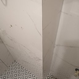 Dobry Remont - Wykończona ściana i podłoga w łazience z białych płytek imitujących marmur i czarno-białych płytek podłogowych z geometrycznym wzorem gwiazdy.