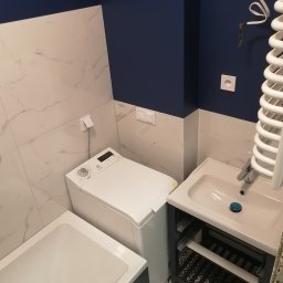 Dobry Remont - Wykończona łazienka w odcieniach bieli i granatu: biała wanna, pralka Electrolux, umywalka z szafką na tle płytek imitujących marmur i granatowej ściany z wystającym kablem.