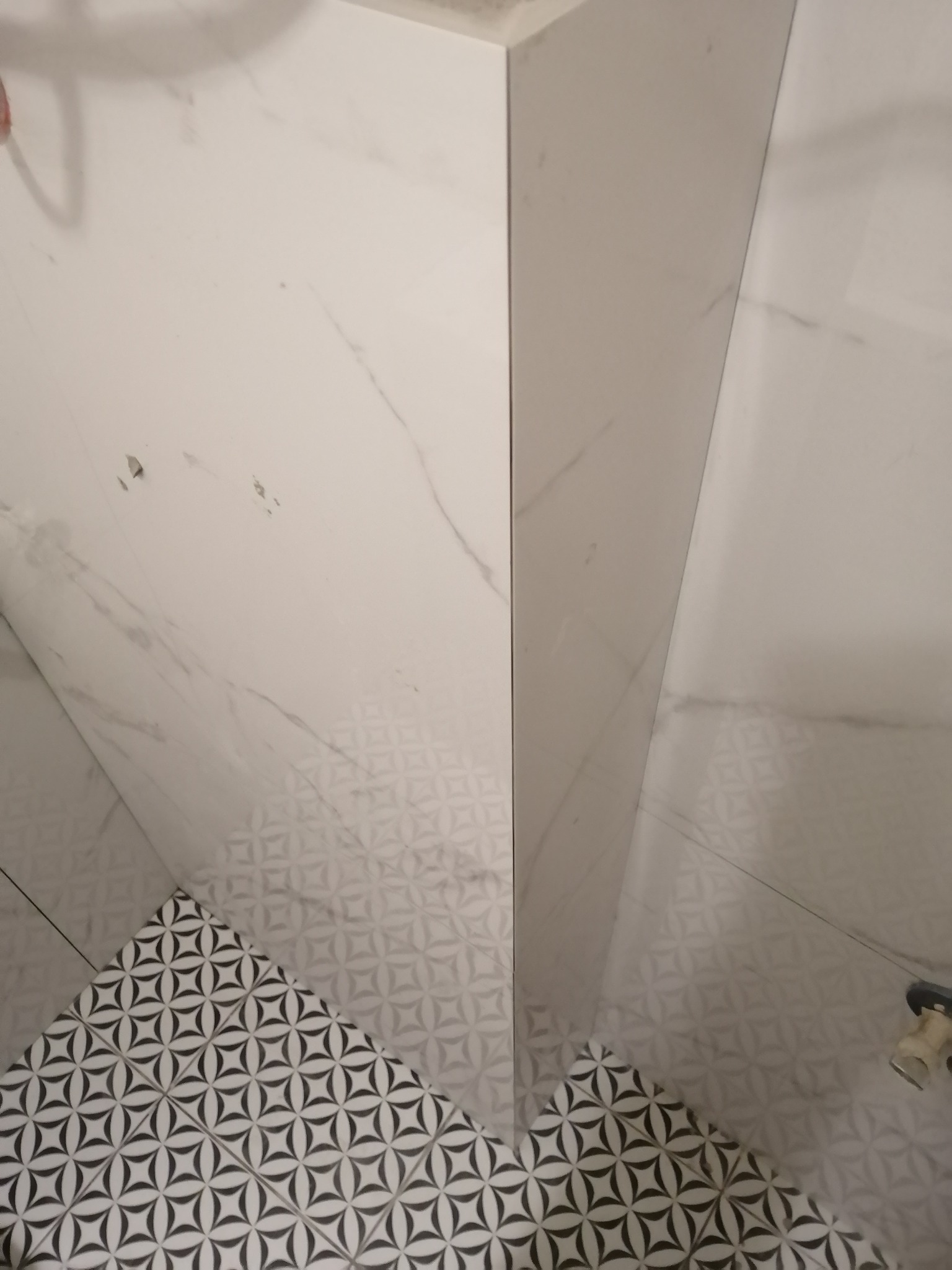 Wykończona ściana i podłoga w łazience z białych płytek imitujących marmur i czarno-białych płytek podłogowych z geometrycznym wzorem gwiazdy.