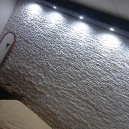 Ściana z dekoracyjnej białej cegły z zamontowanym czarnym panelem oświetleniowym LED w sypialni.