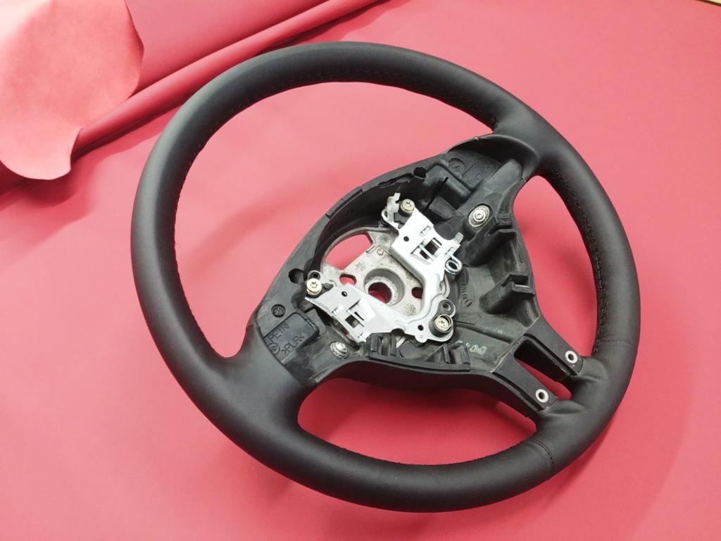 Odnowiona skórzana kierownica samochodowa na czerwonym tle, widoczne szwy i mechanizm mocujący.