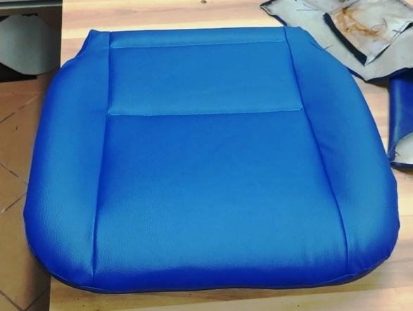 Niebieskie obicie siedziska samochodowego, widoczne szwy i fragmenty materiału w tle.